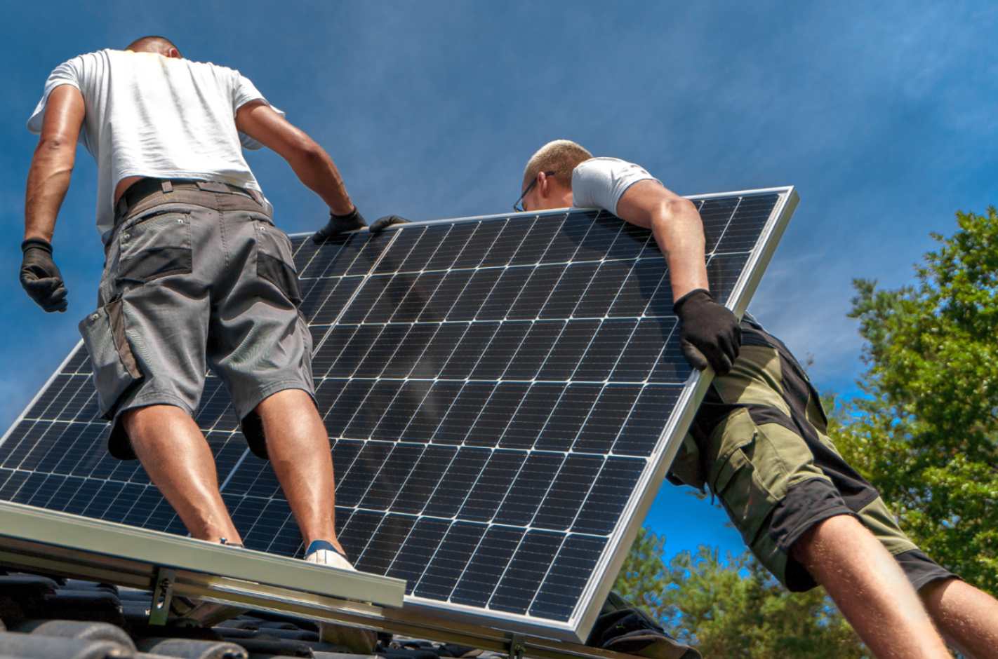 Zwei Männer stehen auf einem Dach mit einer großen Paneele, die sie stützen.